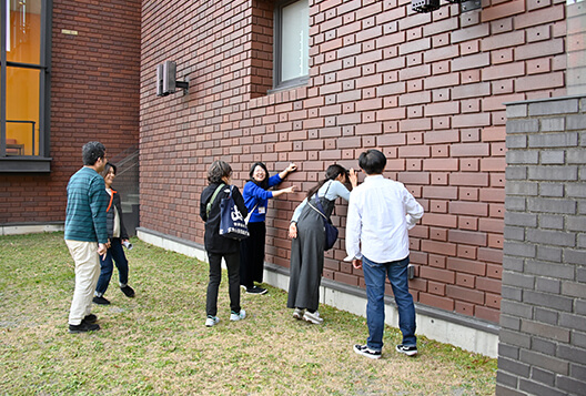 煉瓦色のタイルの外壁を見上げながら観察するグループ