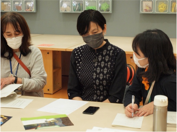 ３人の人がテーブルに向かって座っている写真。テーブルの上には何枚かの紙が置かれている。右側の人はペンを手に持っている。